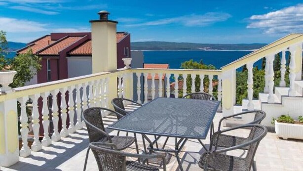 Una terraza con mesa y sillas, baranda blanca y vista al mar.