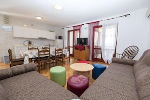 Ett kompakt bostadsutrymme med ett litet kök, en matplats och en sittgrupp med en soffa och sittpallar.