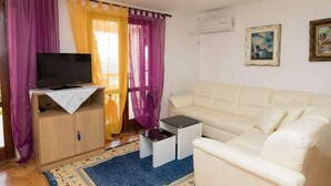 Una sala de estar con un sofá, un televisor sobre un mueble de madera, una mesita y una ventana con cortinas moradas.