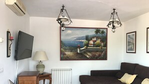 En stue med et stort maleri af et kystlandskab, en sort sofa, et træbord og en lampe.