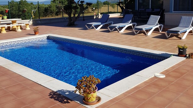 En swimmingpool med liggestole, fliseterrasse og udsigt til bjergene.