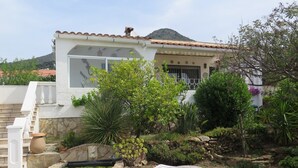 A house with a stone staircase, a white chair, a small table, and a garden with various plants and a pond. - Ref. And28 -  (Rosas / Roses)