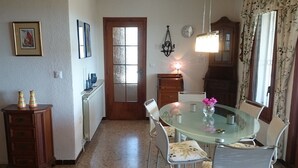 A dining area with a round glass table, white chairs, a wooden cabinet, and a door with frosted glass panels. - Ref. And28 -  (Rosas / Roses)