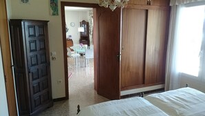 A bedroom with a wooden wardrobe, a bed, and a view of a dining area. - Ref. And28 -  (Rosas / Roses)