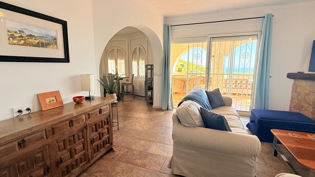A living room with a sofa, a wooden cabinet, a dining area, and a view through a glass door.