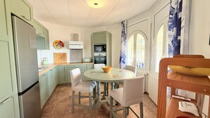 A compact kitchen with a dining area, featuring a round table, chairs, and a wooden bowl.