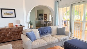 A living room with a sofa, a wooden cabinet, and a dining area visible through an archway.