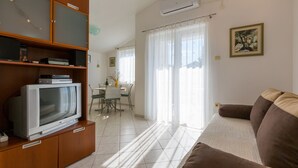 Un salon avec un téléviseur posé sur un meuble en bois, un canapé marron et un coin repas à l’arrière-plan.