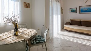Un coin repas avec une table dressée pour deux personnes, une chaise dotée d’un coussin à pois et un vase orné de branches.