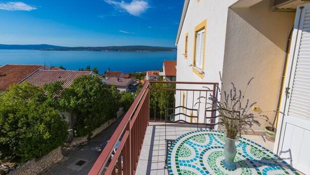 Un balcon doté d’un sol carrelé, d’une plante en pot et offrant une vue sur une étendue d’eau et des bâtiments éloignés.