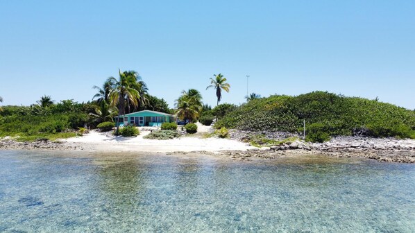 Una propiedad frente a la playa con una casa, agua turquesa cristalina y exuberante vegetación.