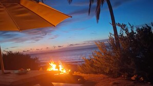 A beach scene with a fire, a wooden table, and a beach umbrella.