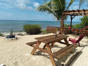 Una mesa de picnic de madera y un banco sobre una playa arenosa, con vista al océano.