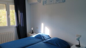 Un dormitorio con cama, mesita de noche, lámpara y ventana con cortinas.