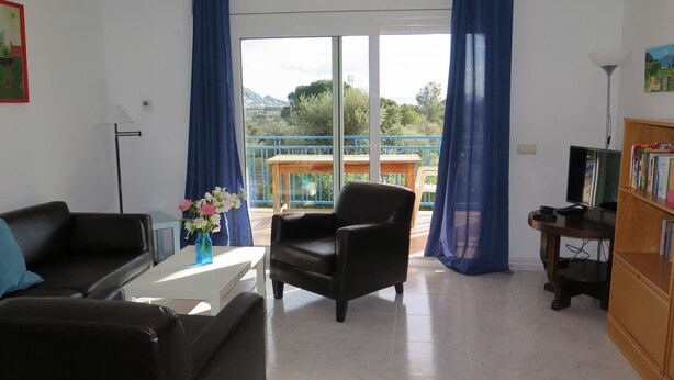 Una sala de estar con un sofá, una silla, una mesa de centro con un jarrón de flores, un televisor y una estantería.
