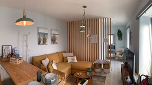 A modern living room with a wooden dining table, a sofa, and a TV. There are decorative baskets and a small plant on the floor. - Villaverde Azores (Ponta Delgada)