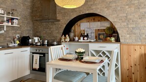 A kitchen with a brick wall, wooden ceiling, and a hanging light fixture. There is a table with chairs and a sign about wines. - Villaverde Azores (Ponta Delgada)