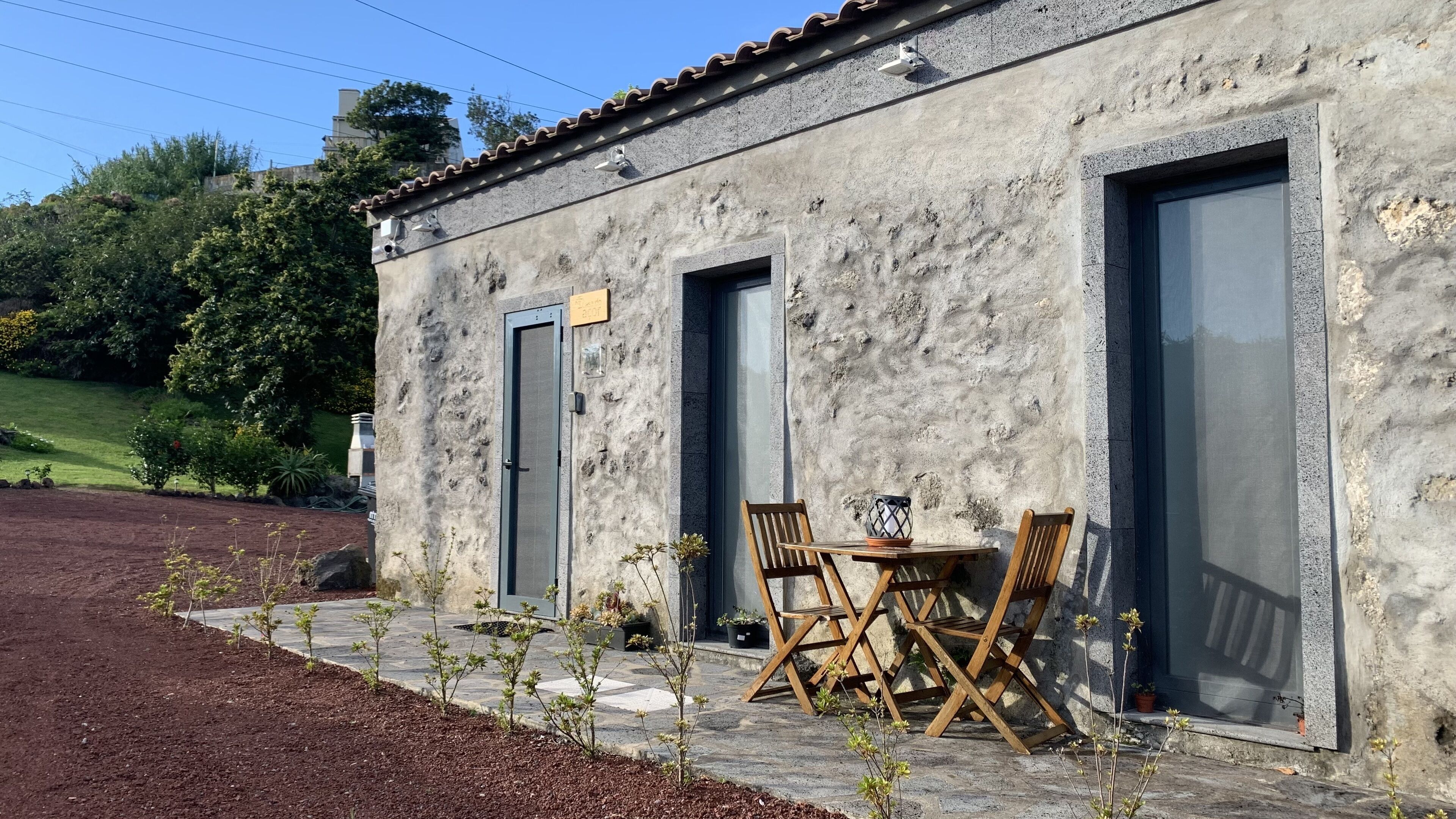 A rustic building with a stone facade, two doors, and a small patio area with a table and chairs.
