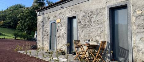 A rustic building with a stone facade, two doors, and a small patio area with a table and chairs.