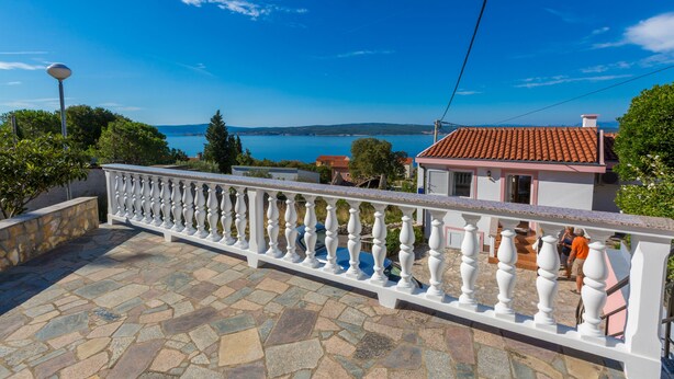 Een balkon met stenen bestrating en een witte balustrade met uitzicht op de kust.