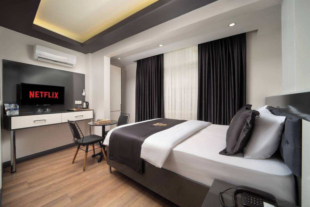 Une chambre d’hôtel moderne équipée d’un lit, d’un bureau avec un ordinateur, d’une chaise et d’un téléviseur affichant le logo « NETFLIX ».