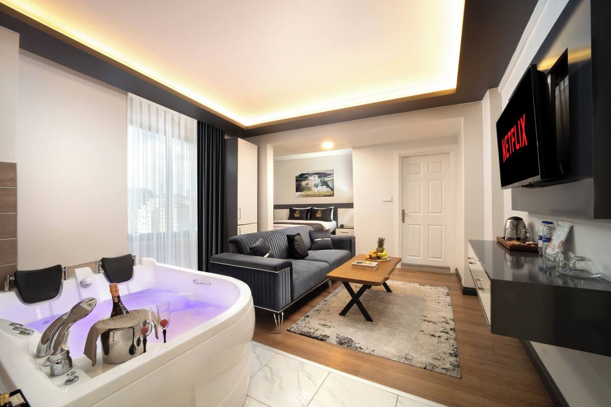 Un salon moderne avec une grande baignoire blanche, un canapé gris, une table basse en bois et un téléviseur à écran plat fixé au mur.