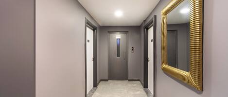 A hallway with a large golden-framed mirror, grey walls, and a door at the end.