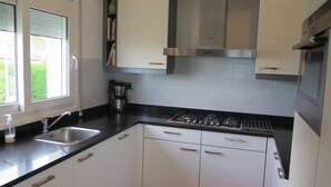 A modern kitchen with white cabinets, a gas stove, a coffee maker, and a window with blinds. - Ref. Nav44 -  (Rosas / Roses)