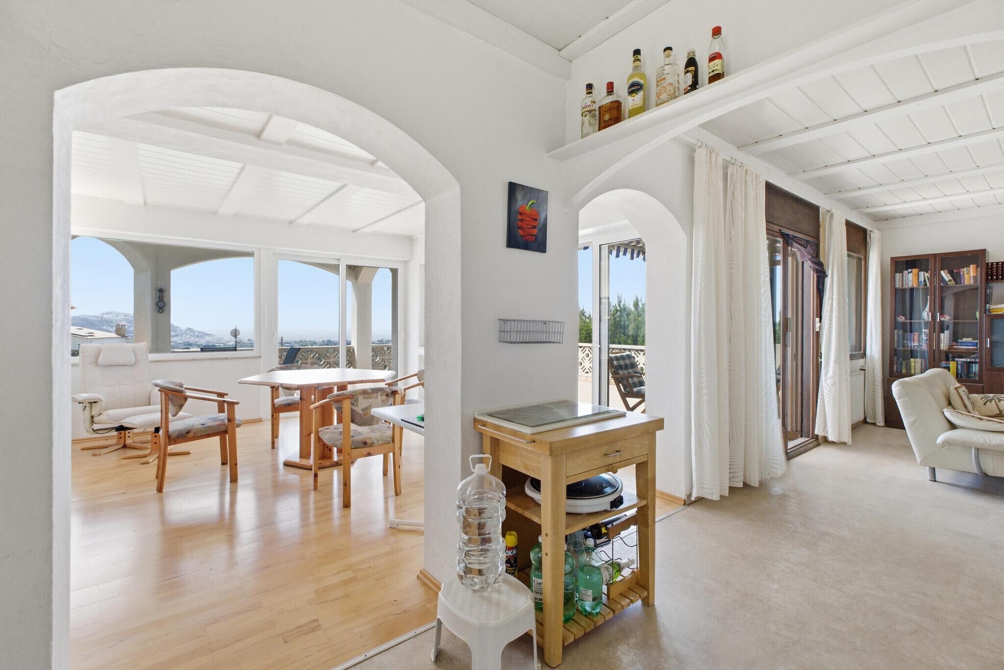 A spacious living area with a dining set, a water dispenser, and a view through an arched doorway.