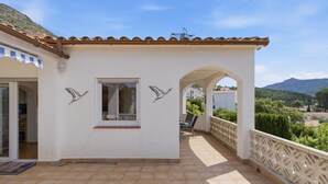 A building with a tiled roof, a balcony with a railing, and a view of a mountainous landscape.