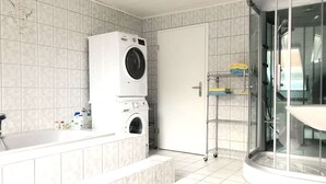 Une salle de bain moderne dotée d’un lave-linge et d’un sèche-linge intégrés, d’une douche à parois de verre et d’un sol carrelé.