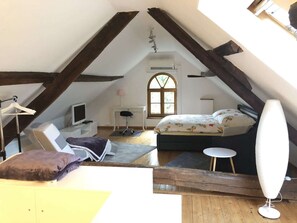 A cozy attic bedroom with a bed, desk, and chair, wooden beams, and a window. - Cozy apartment on a listed Sturmhof (Grefrath)