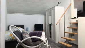 Une petite pièce comprenant un lit, une chaise en osier, un bureau et un escalier.