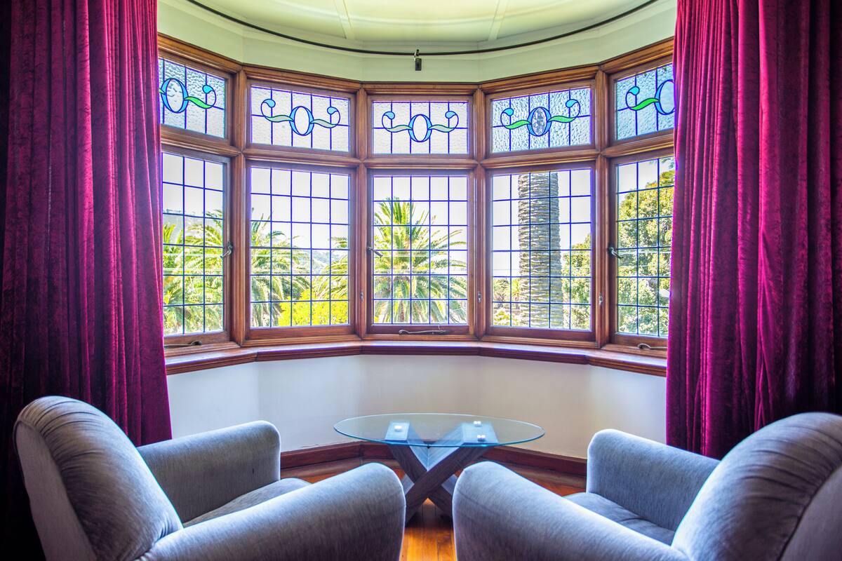Une baie vitrée ornée de vitraux, deux fauteuils et une table en verre.