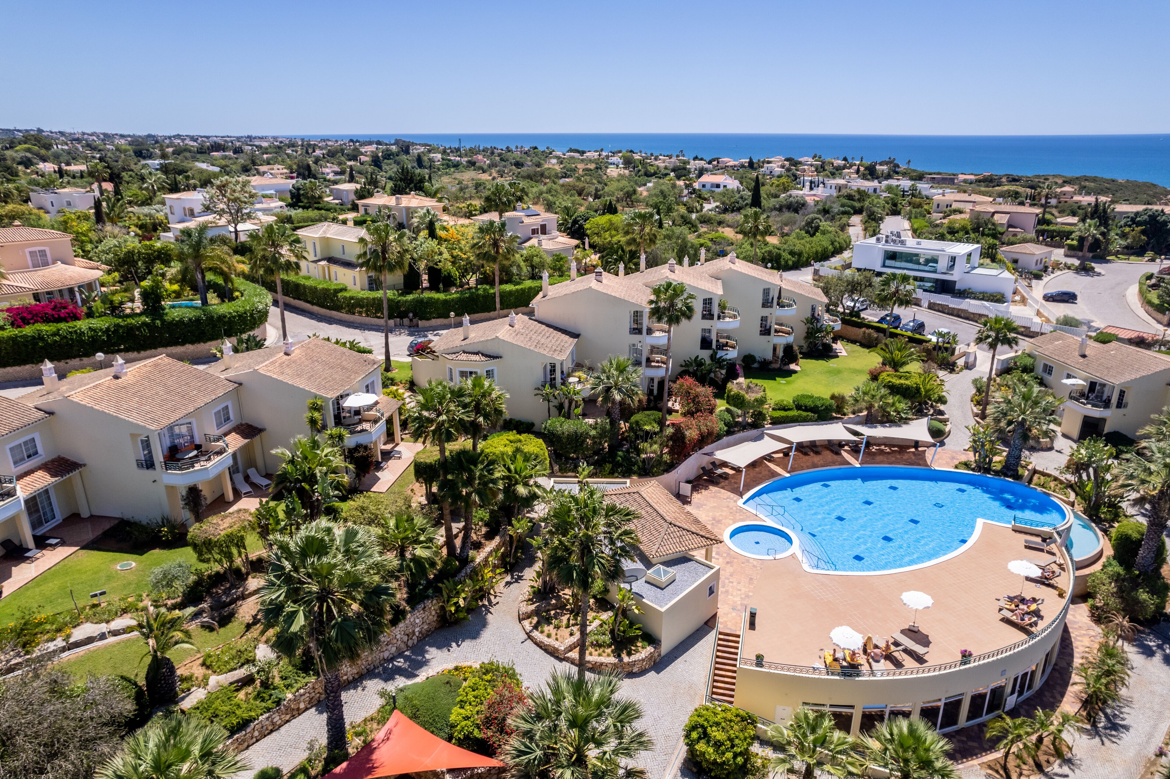 Zona residencial con una gran piscina rodeada de palmeras y vistas despejadas al mar.