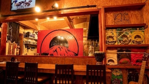 A bar area with wooden chairs, a large painting of a mountain, and shelves with various items including a guitar. - Youtei - Hostel (Rusutsu)