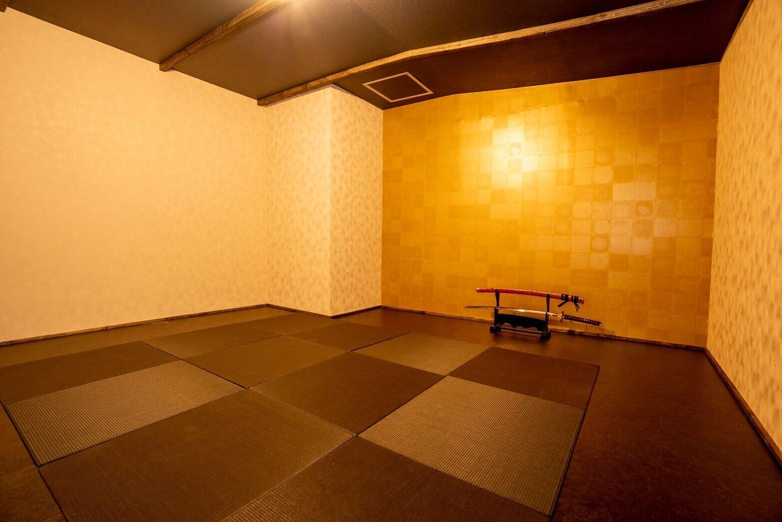 A room with tatami mat flooring, a wooden ceiling, and a wall with a geometric pattern.
