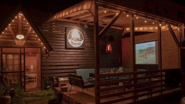 A rustic wooden building with a sign reading "YouTel" and a projection screen displaying a landscape. - Youtei - Hostel (Rusutsu)