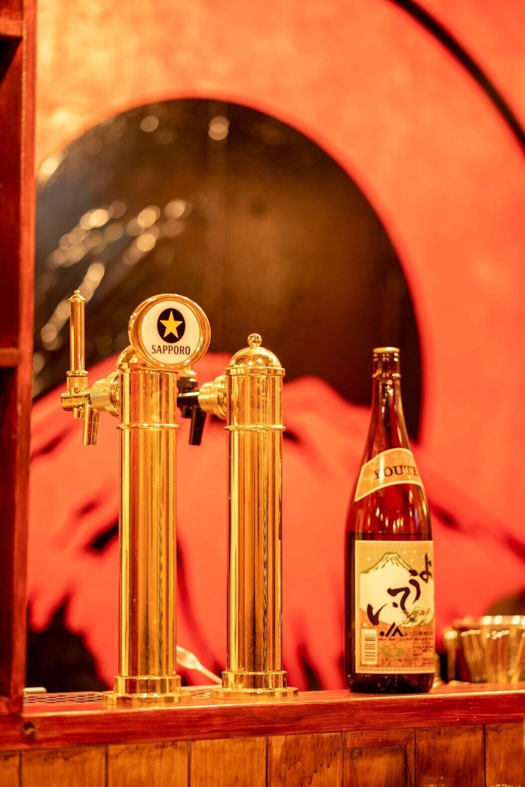 A bar area with a gold-colored beer tap labeled "Sapporo" and a bottle of "YOUT" beer.