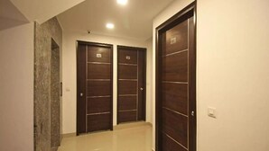 Un couloir avec trois portes en bois sombre, un plancher ciré et un interrupteur sur le mur.