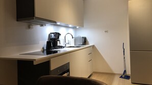 A compact kitchenette with a coffee maker, toaster, and microwave. There is a sink with a faucet, and a broom leaning against the wall. - The Meridian (Tromsø)