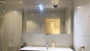 A modern bathroom with a glass shower enclosure, a white sink with a mirror above it, and a towel hanging on the wall. - The Meridian (Tromsø)