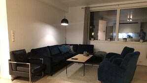 A modern living room with a dark blue sofa, a small coffee table, and a floor lamp. - The Meridian (Tromsø)
