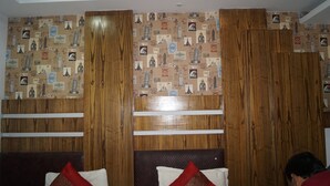 A hotel room with a wooden headboard, a patterned wallpaper with various landmarks, and two beds with red and white pillows. - Hotel Lord Krishna Palace (New Delhi)
