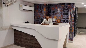 A reception desk with a modern design, a patterned wall in the background, and a person standing behind it. - Hotel Lord Krishna Palace (New Delhi)