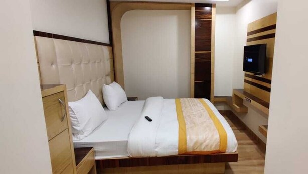 A bedroom with a bed, a TV mounted on the wall, and a wooden wardrobe. - Hotel Lord Krishna Palace (New Delhi)
