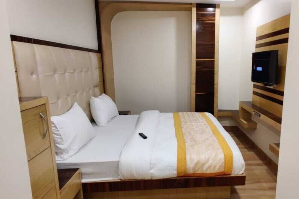A bedroom with a bed, a TV mounted on the wall, and a wooden wardrobe.