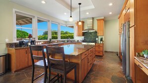 A spacious kitchen with a large island, wooden cabinets, and a stainless steel refrigerator.