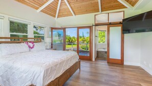 A bedroom with a large bed, wooden ceiling, and a view of a tropical landscape through the sliding glass doors.