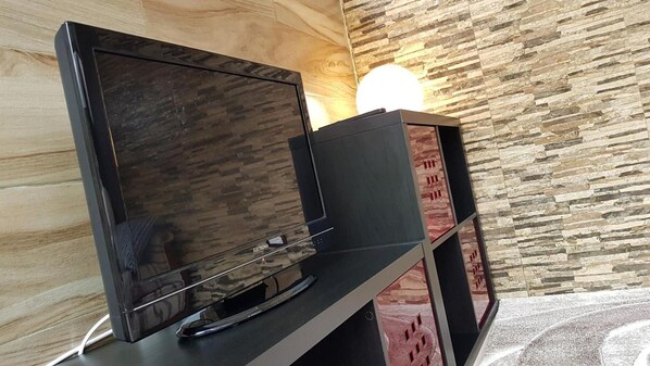 A flat-screen TV on a stand with a wooden wall and a stone-patterned wall in the background.